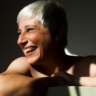 A smiling, half-shadowed silver-haired woman leaning on the back of a light green chair