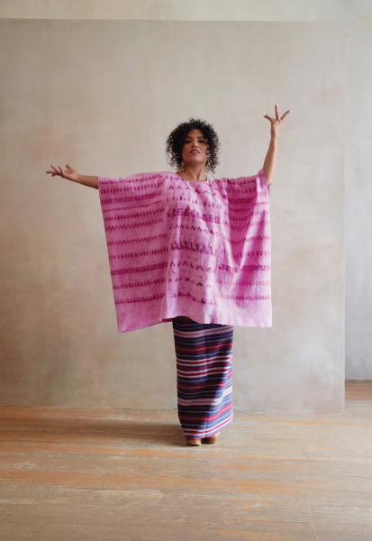 an afro mexican woman standing proudly with her hands raised wearing a pink patterned poncho and floorlength striped skirt